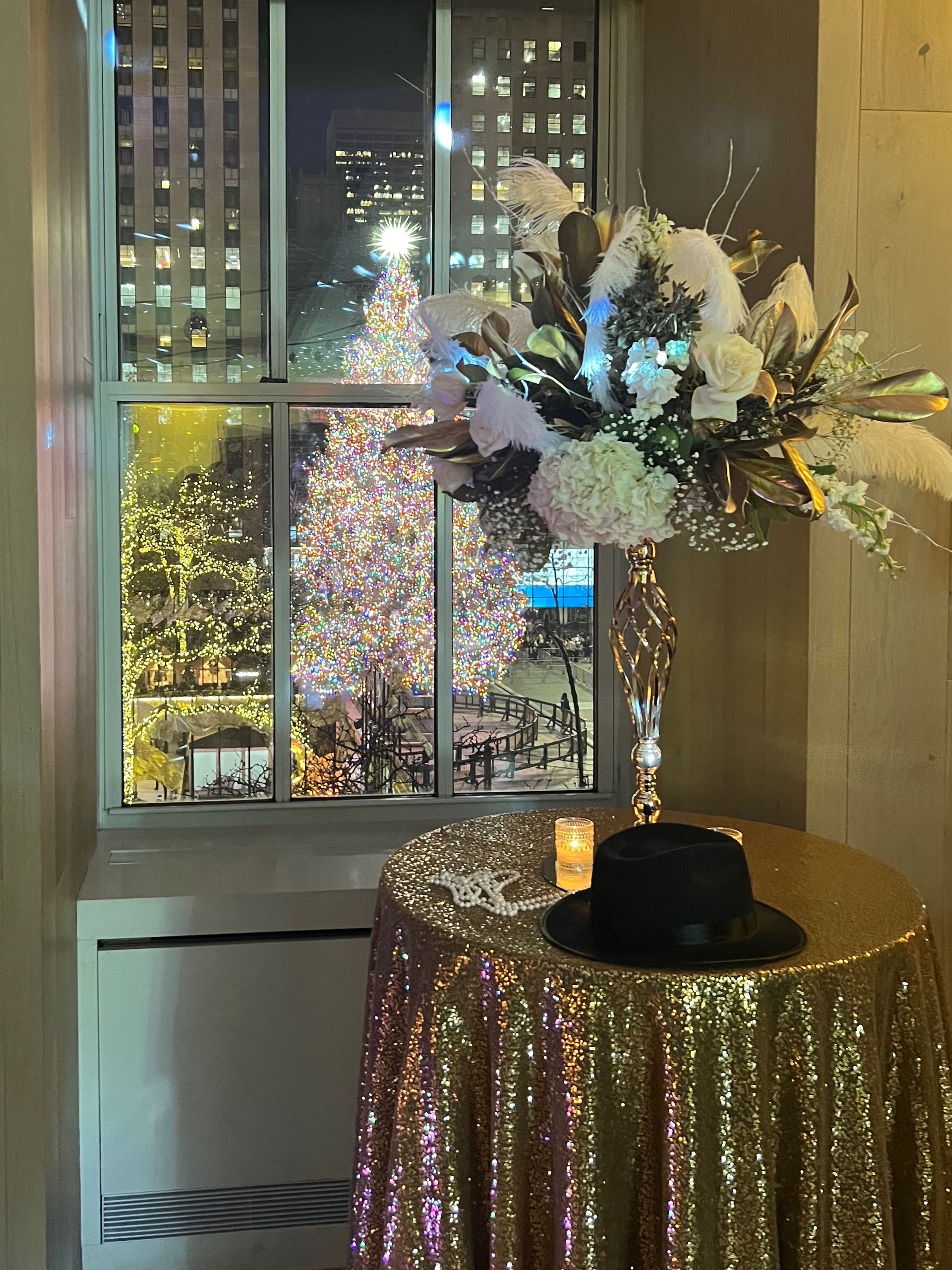 EQX City Catering Event Space at Rockefeller Center - A table with a hat and flowers on it in front of a window with a christmas tree in the background.
