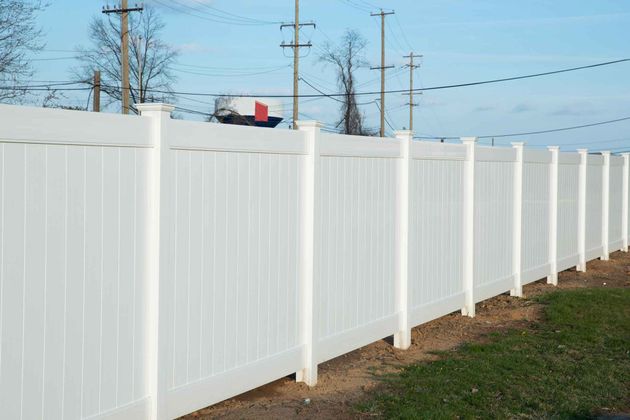 White picket fence along a sidewalk beside a grassy yard and stone house exterior