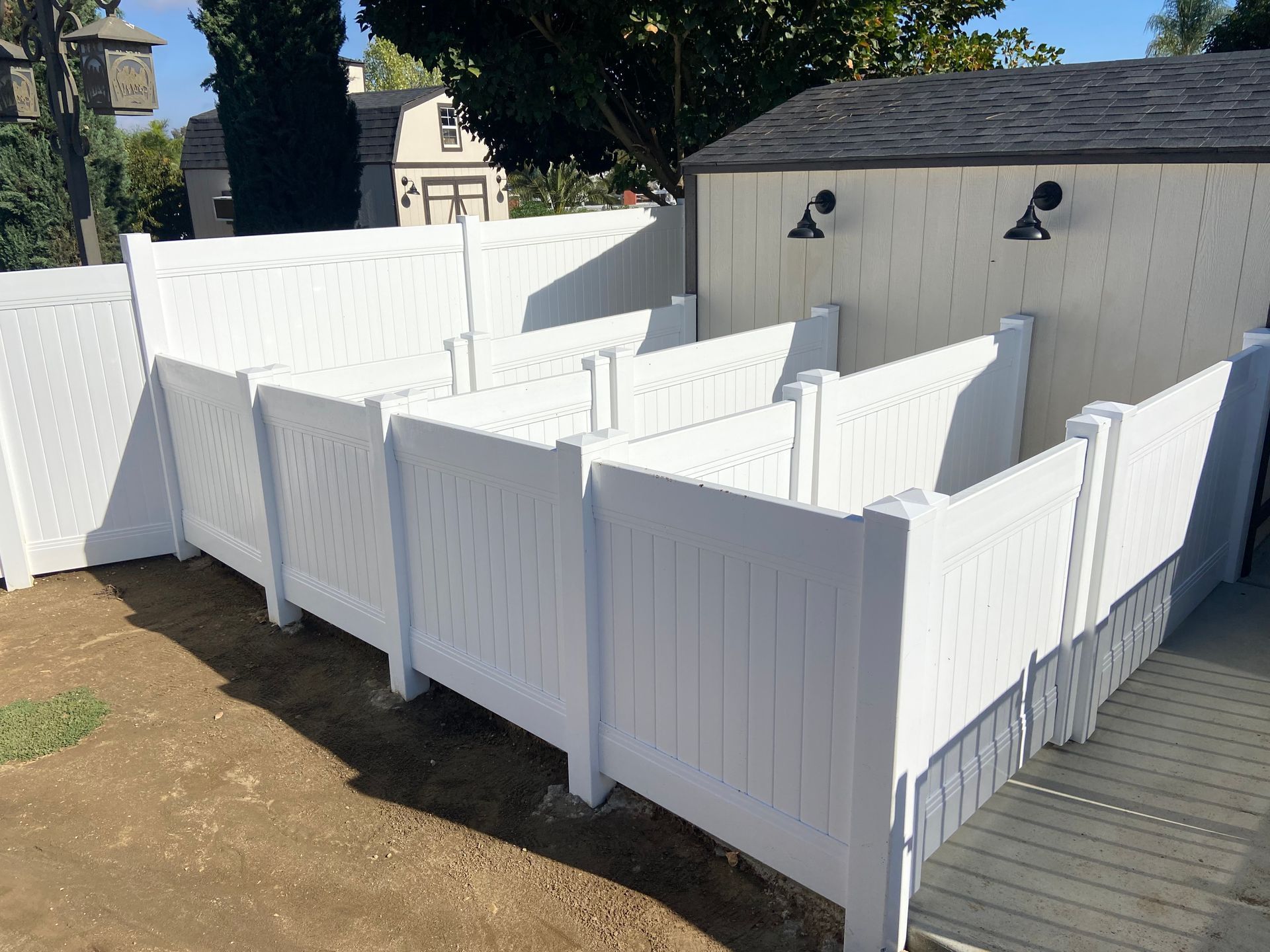 White fenced outdoor pens beside a shed and wooden deck in a sunny backyard