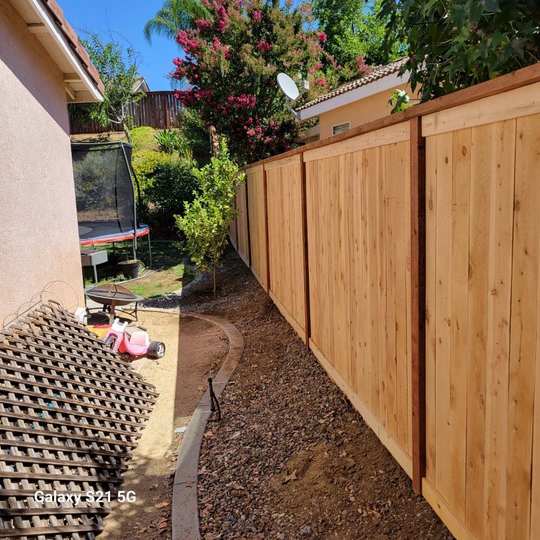 Narrow side yard with a new wooden fence, dirt path, and house walls on both sides.