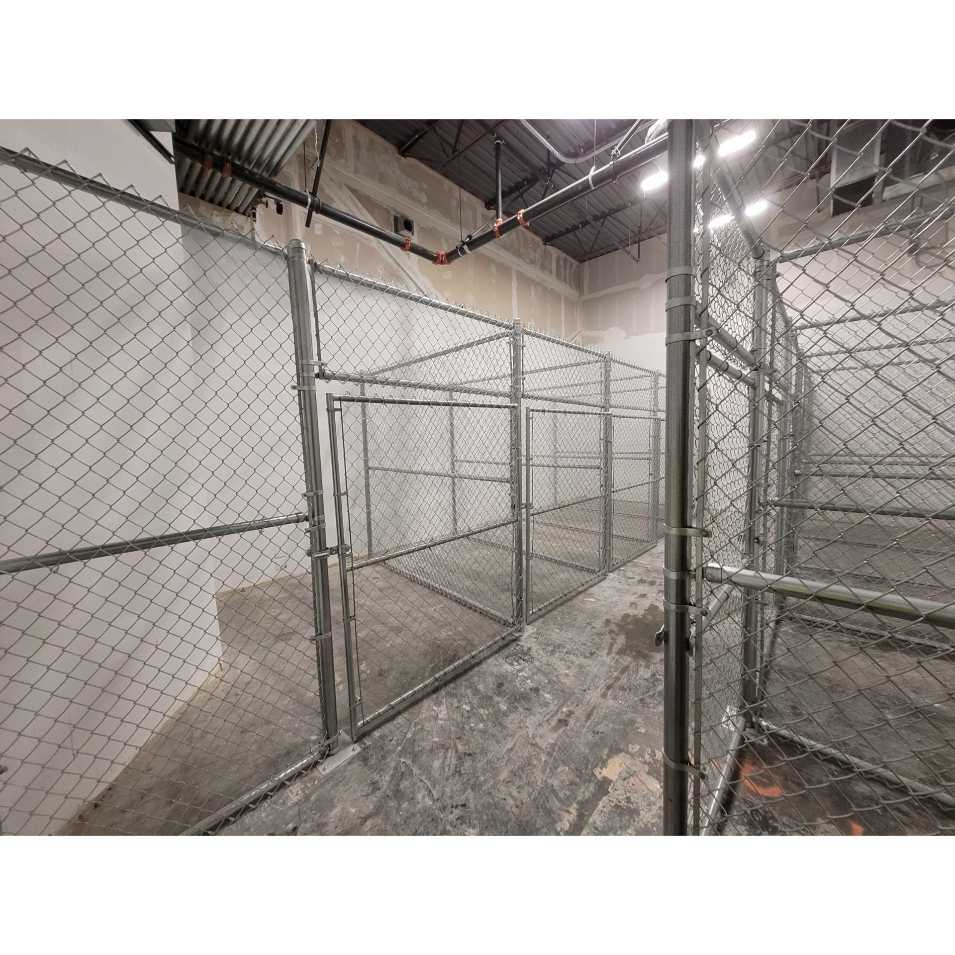 Chain-link fenced industrial corridor with concrete floor and overhead lights inside a warehouse-like space