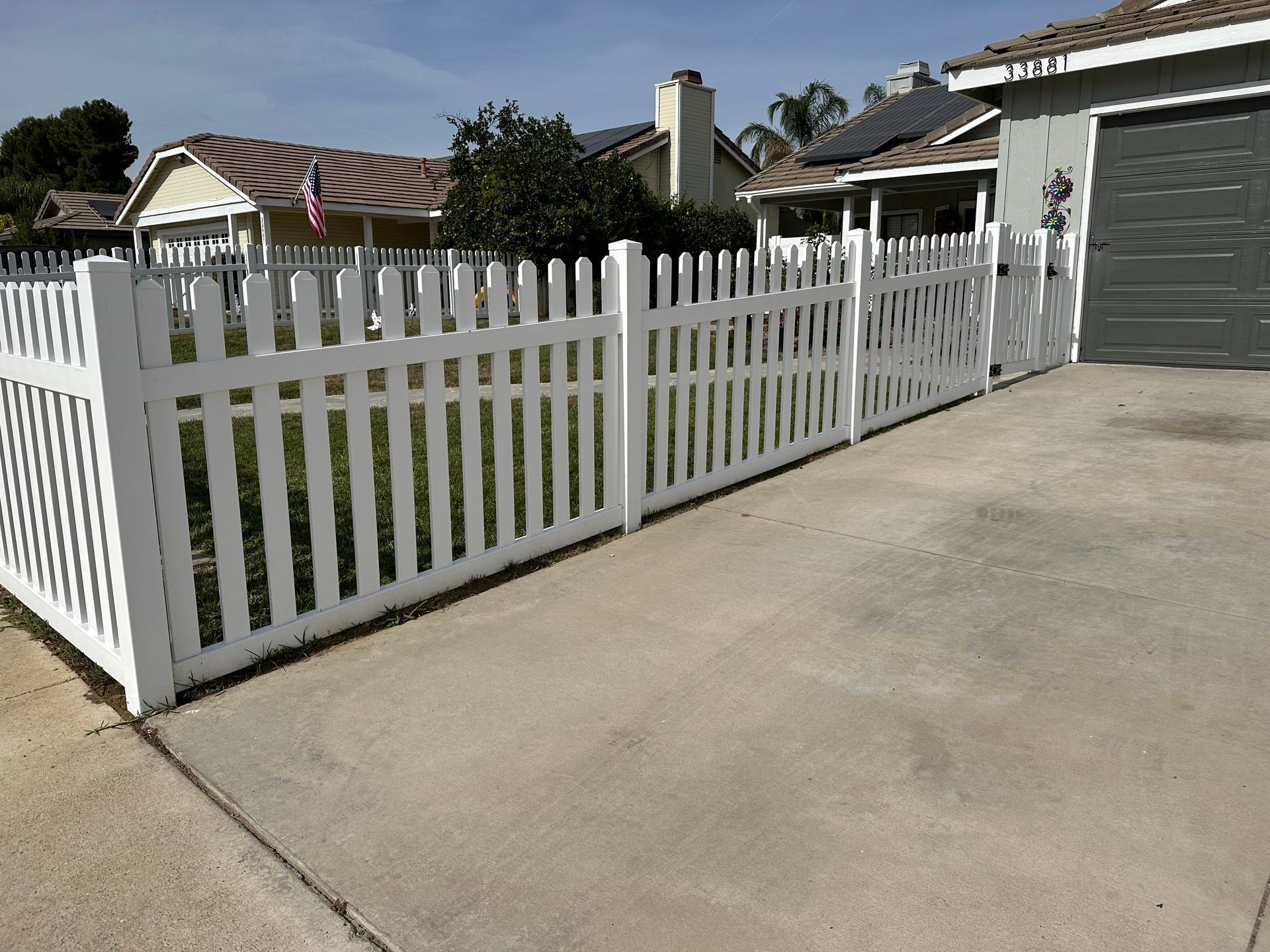White picket fence along a concrete driveway beside a gray garage in a suburban yard