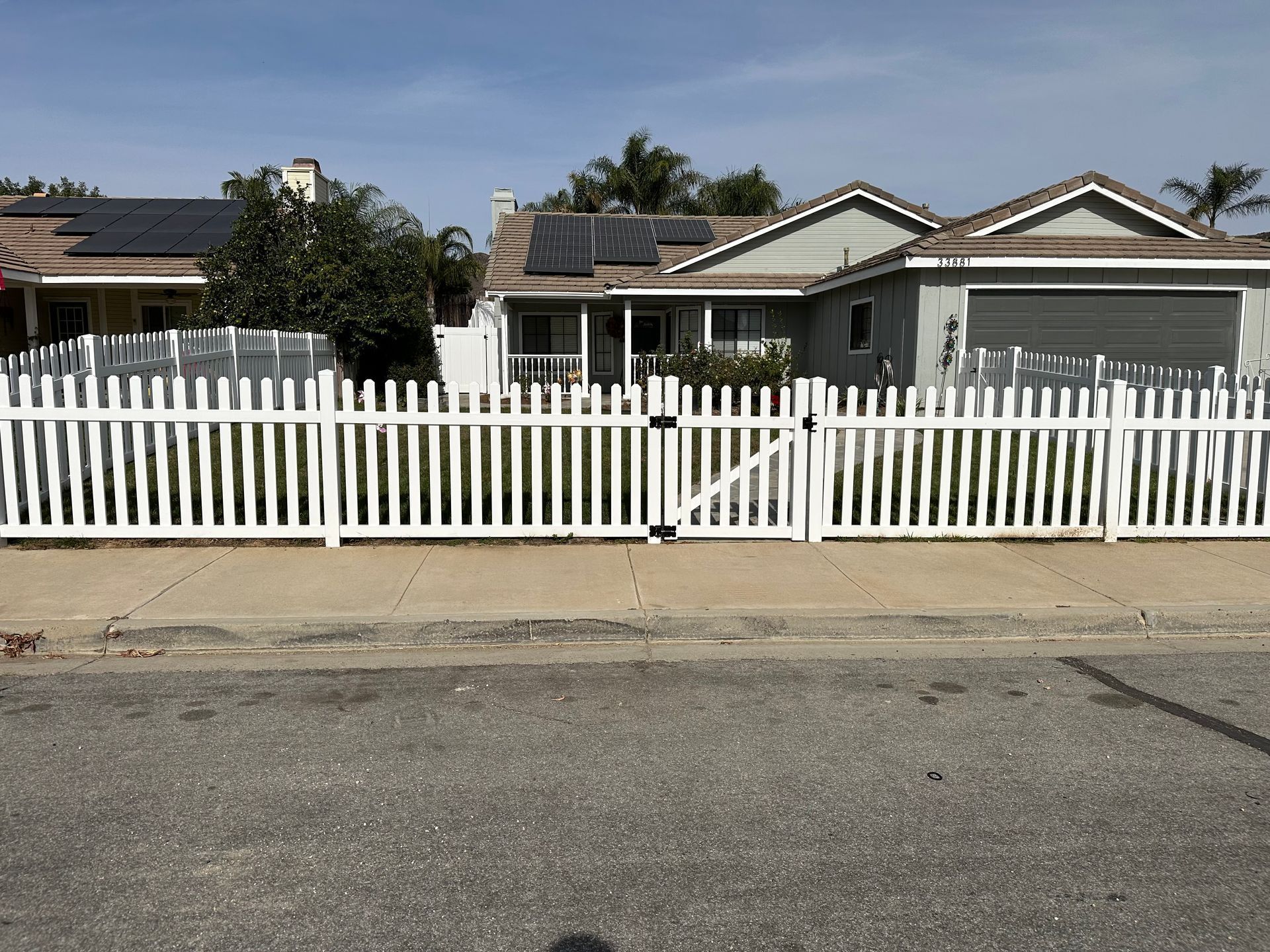 White picket fence in front of a suburban house with a driveway and street.