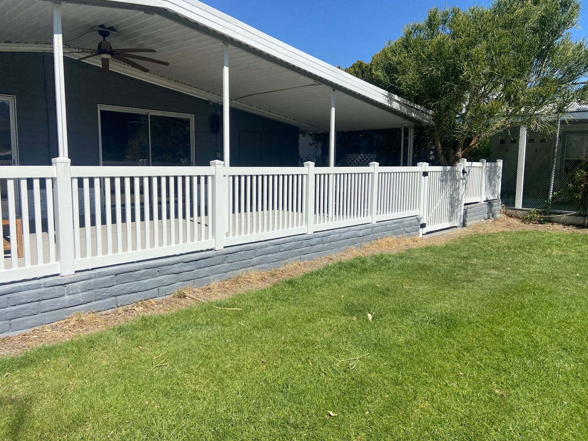 White railing porch along a house with a green lawn and trees in front under a clear blue sky