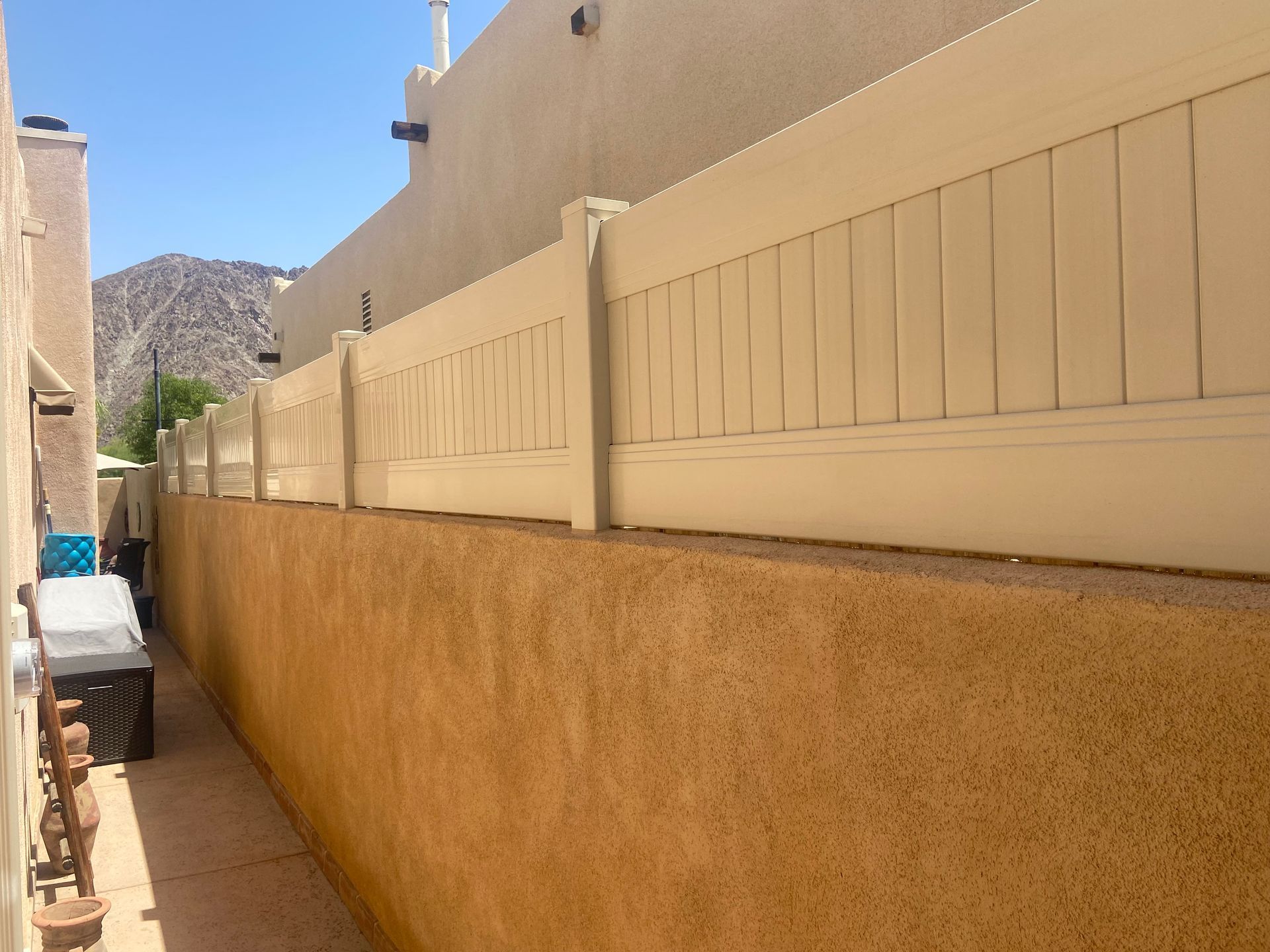 Narrow outdoor alley with beige stucco walls and a distant mountain under a clear blue sky