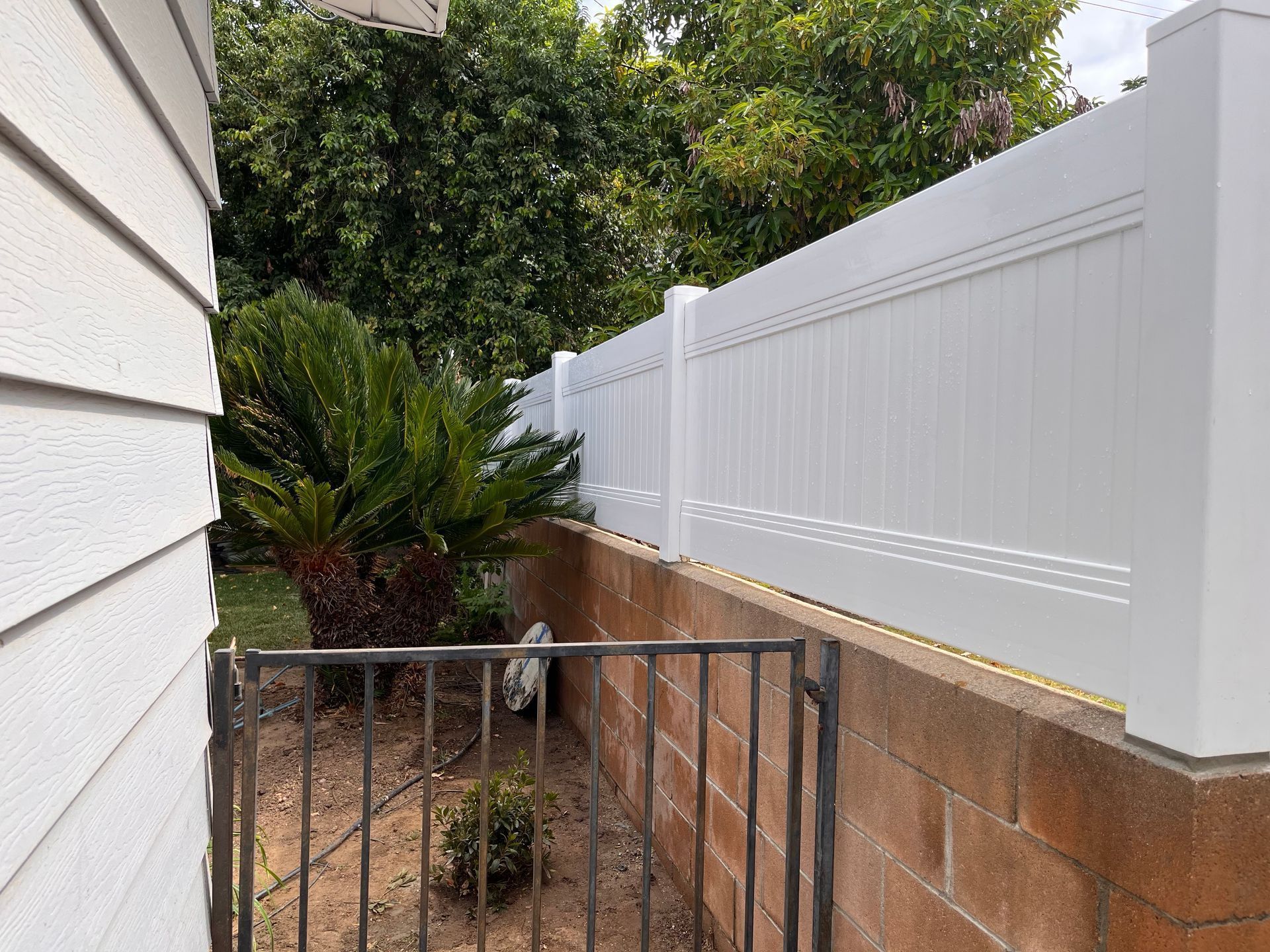 Narrow side yard with white fence, brick wall, and black metal gate beside a house