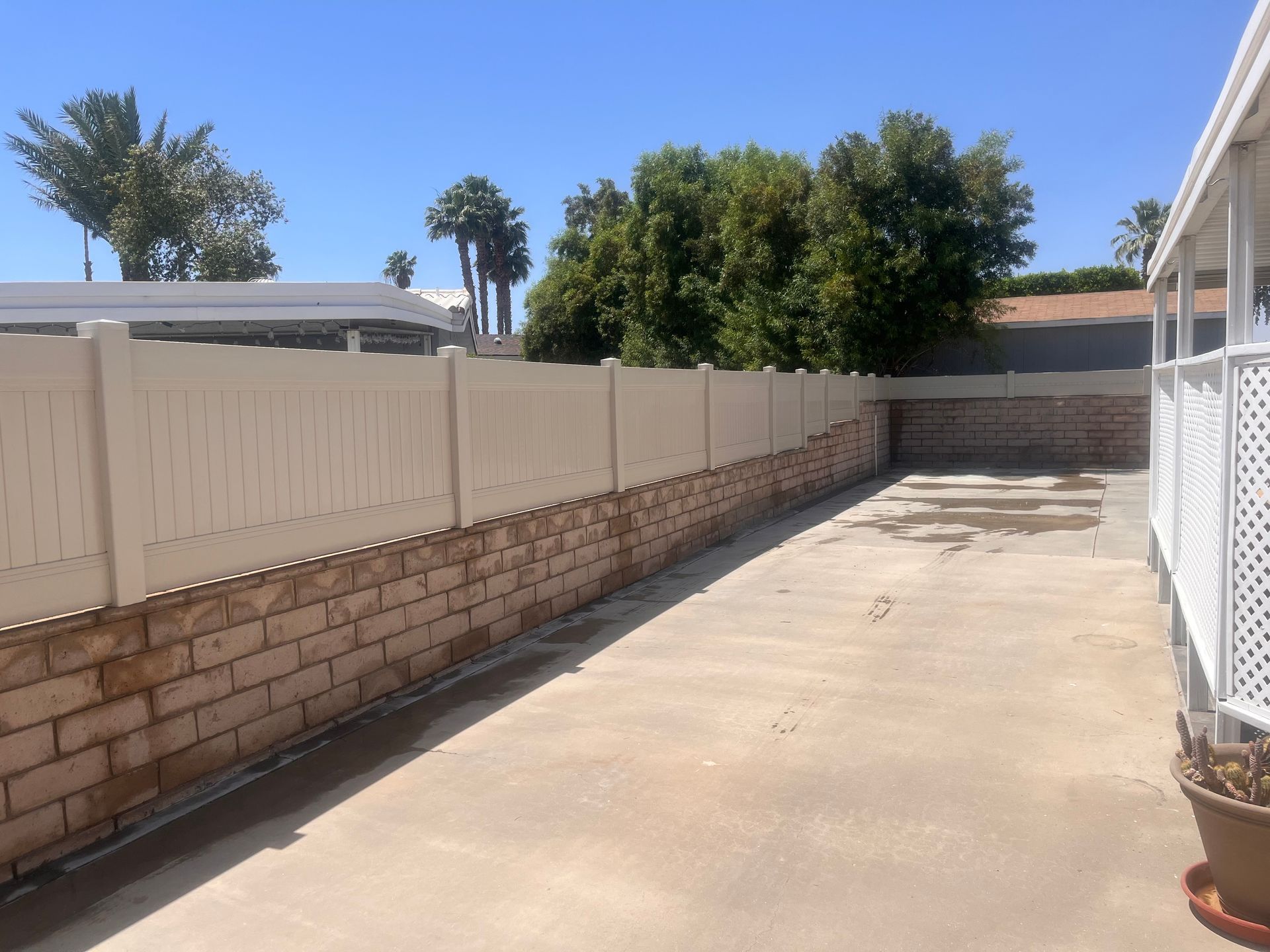 Narrow concrete driveway beside a brick-and-beige fence under a bright blue sky
