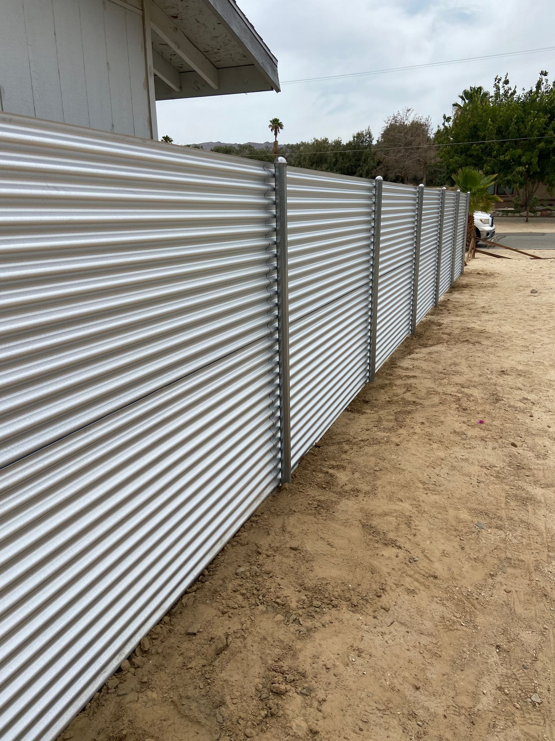 Corrugated metal fence along a dirt path beside a white building