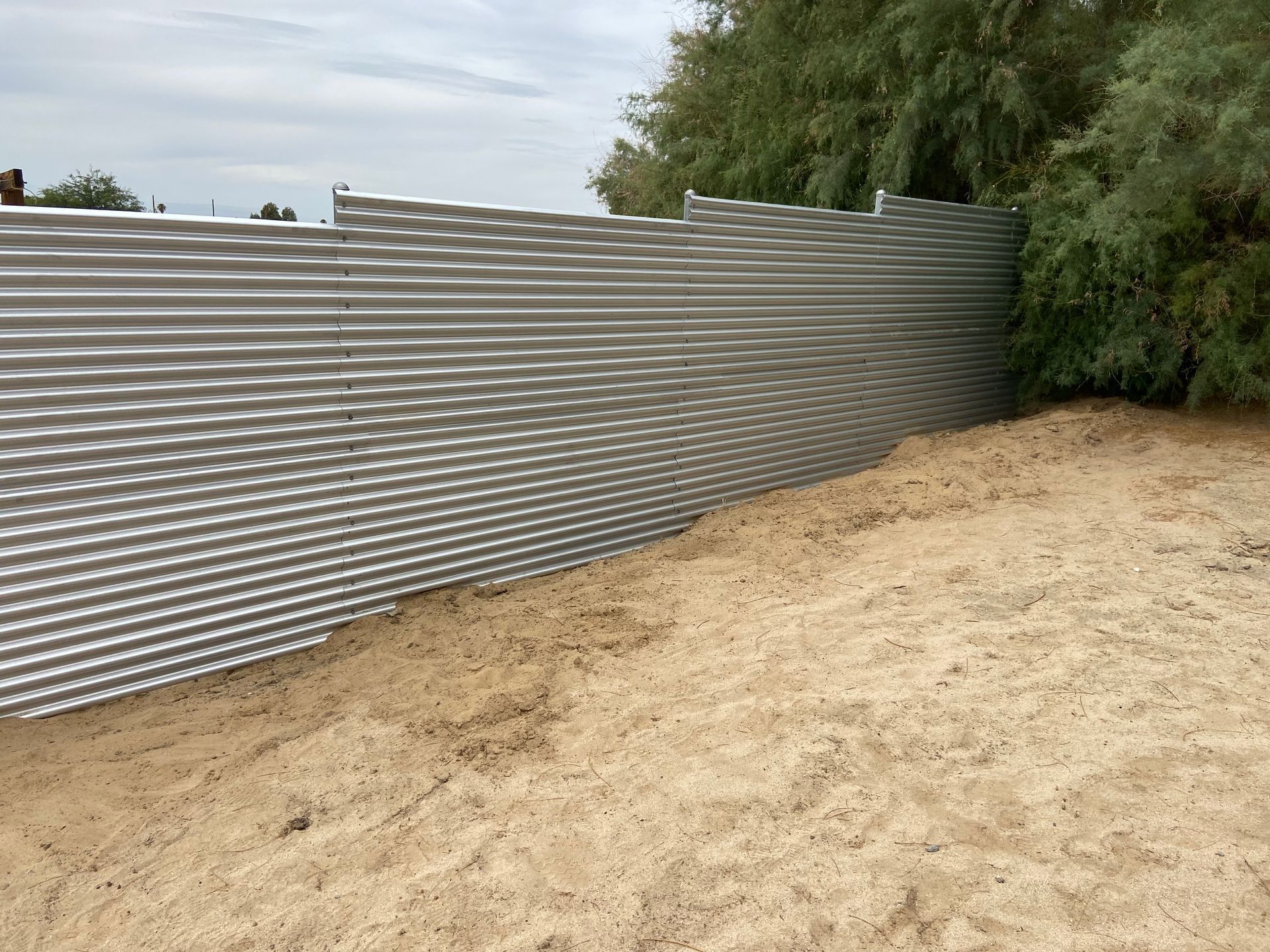 Corrugated metal fence beside a sandy dirt path and trees