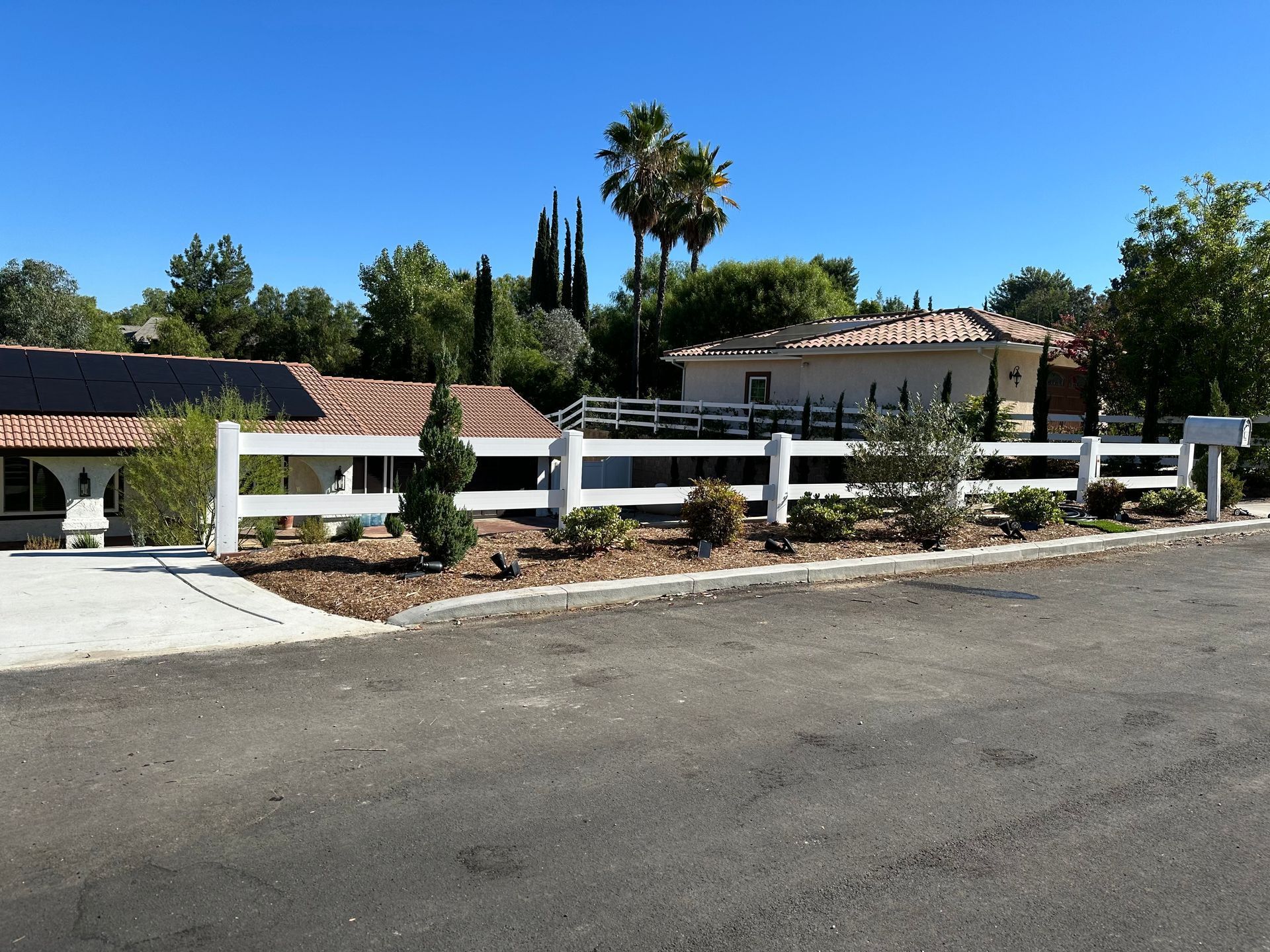 Suburban house with white fence, palm trees, and a driveway on a sunny day