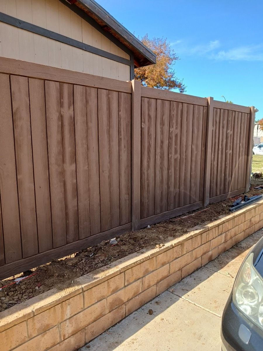 Brown wooden fence beside a tan retaining wall along a driveway under a blue sky