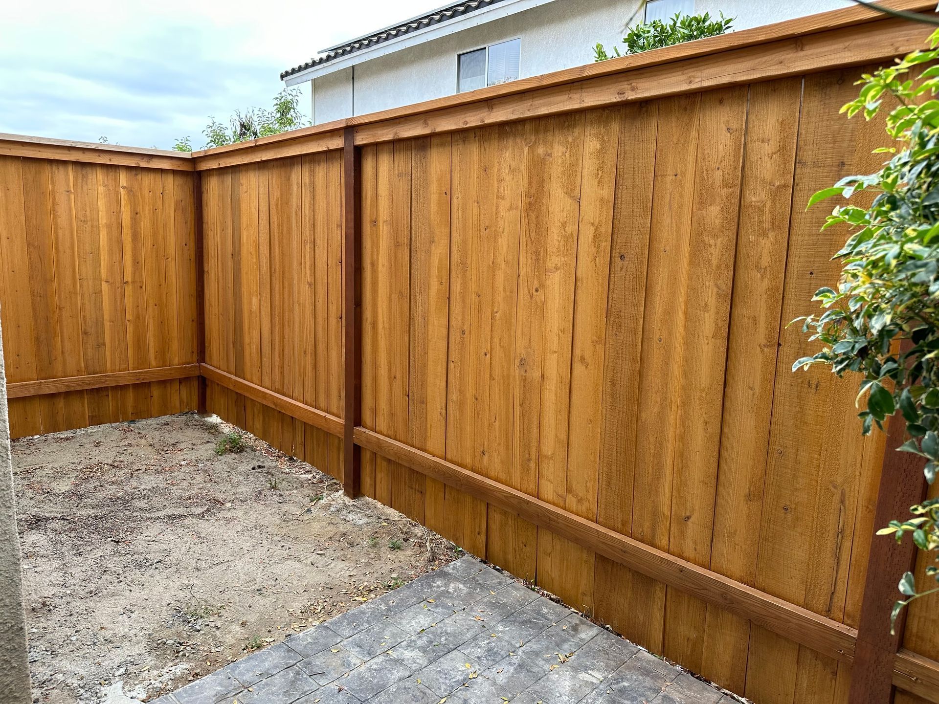 Wooden privacy fence enclosing a small backyard with a concrete patio and dirt area