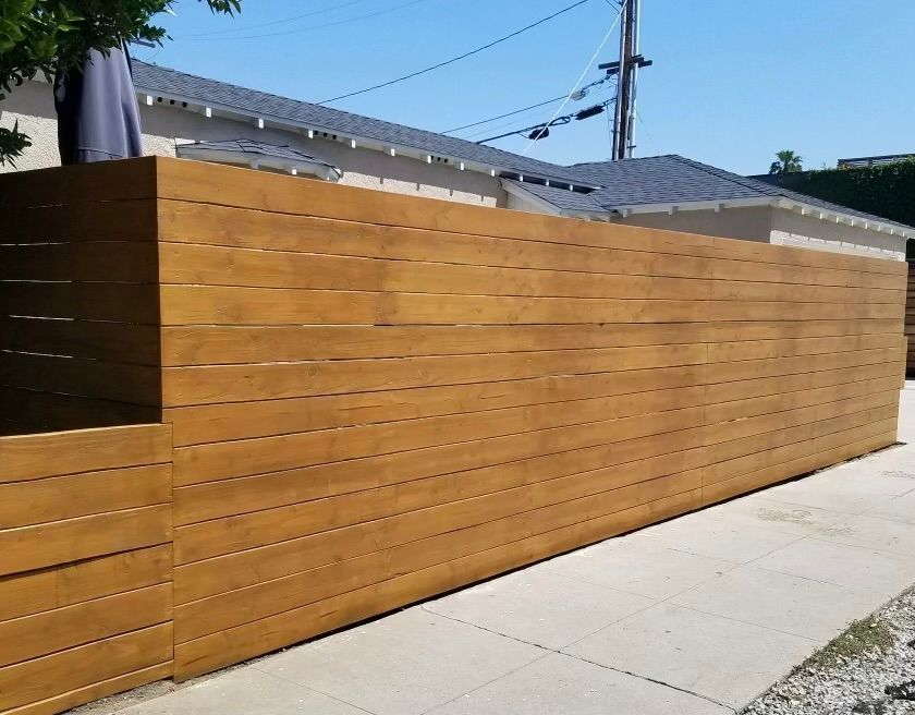 Wooden privacy fence along a concrete sidewalk beside a house under a clear blue sky