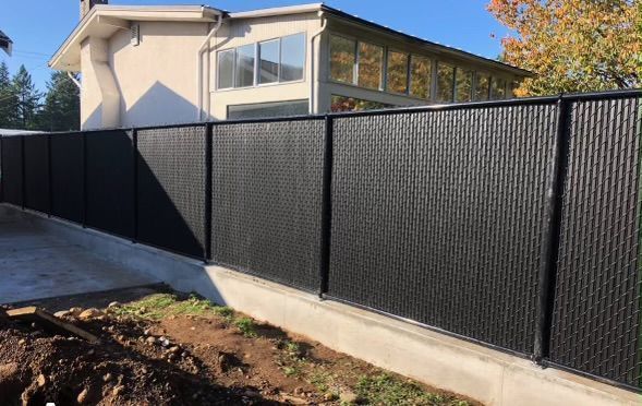 Black metal fence along a concrete retaining wall beside a house and driveway under a clear blue sky