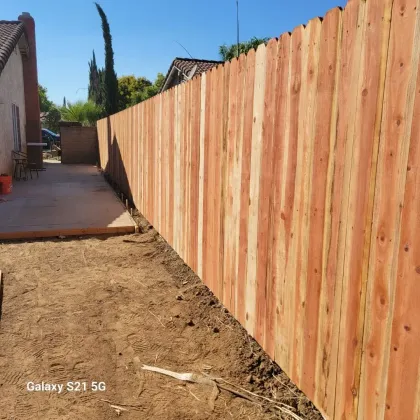 Long wooden fence beside a dirt yard and patio under a blue sky
