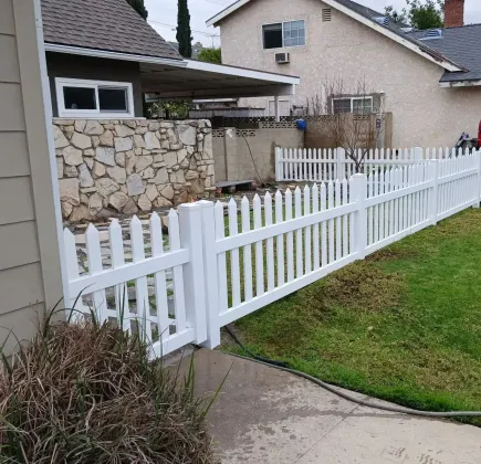 White picket fence along a sidewalk beside a grassy yard and stone house exterior