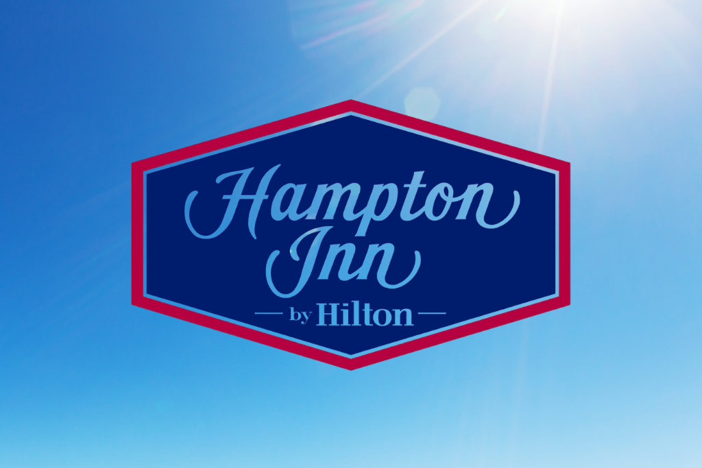 Hampton Inn by Hilton logo on a blue sky background with sun flare