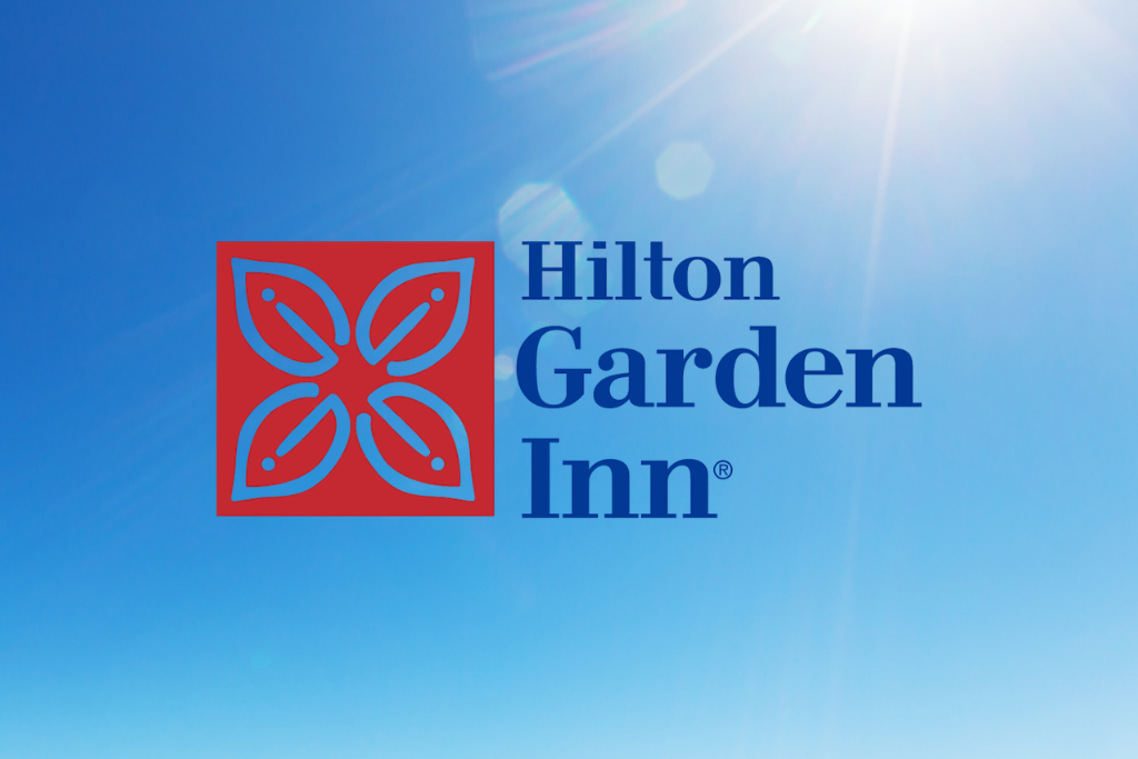 Hilton Garden Inn logo on a blue sky background with sun flare