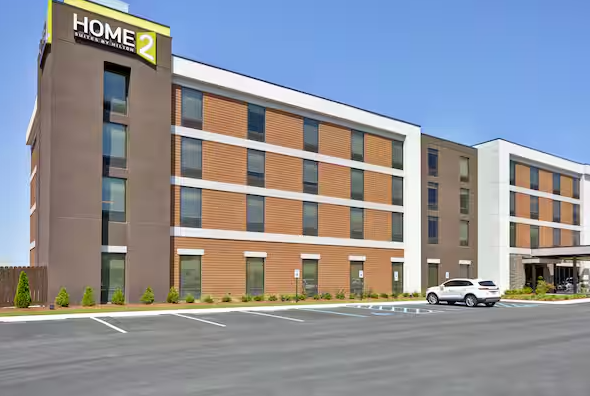 Modern brick hotel exterior with a “HOME2” sign and a parking lot in front