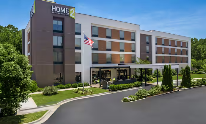 Modern hotel exterior with brown and white facade, U.S. flag, and landscaped entrance drive