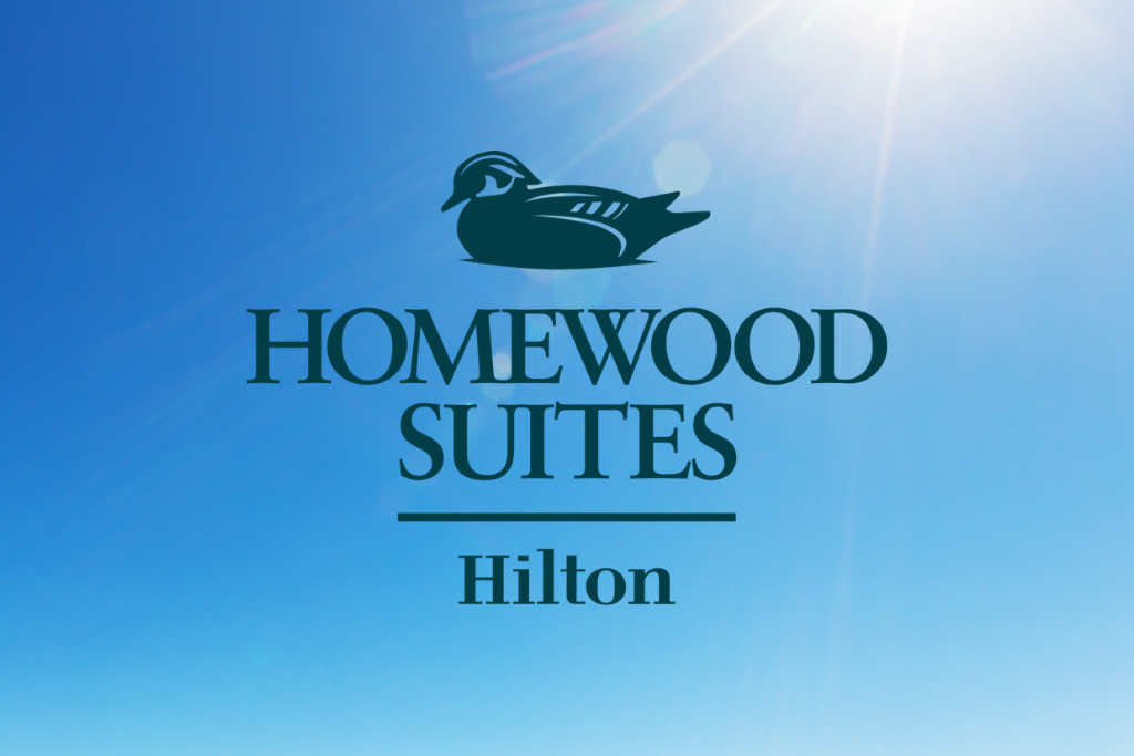 Homewood Suites by Hilton logo on a blue sky background with sun flare