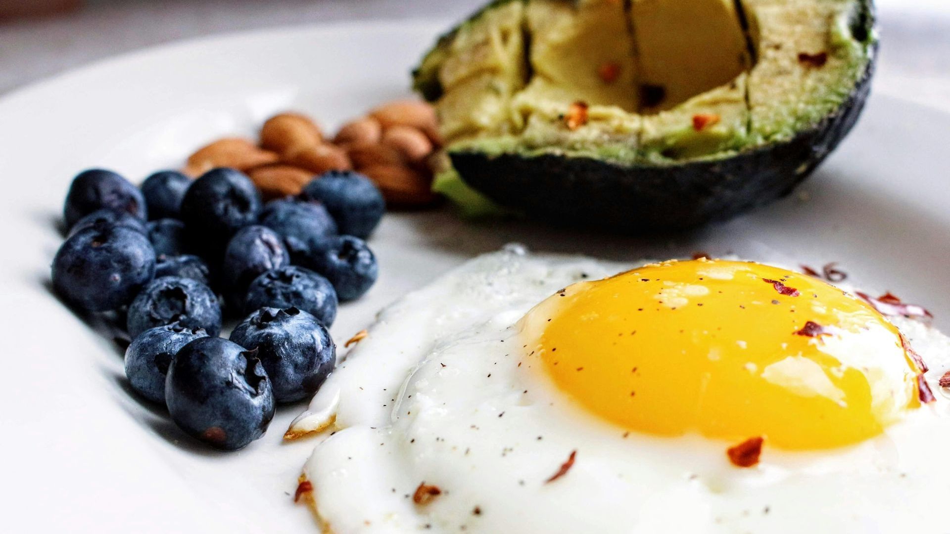 A plate of food with eggs , blueberries , avocado and almonds.