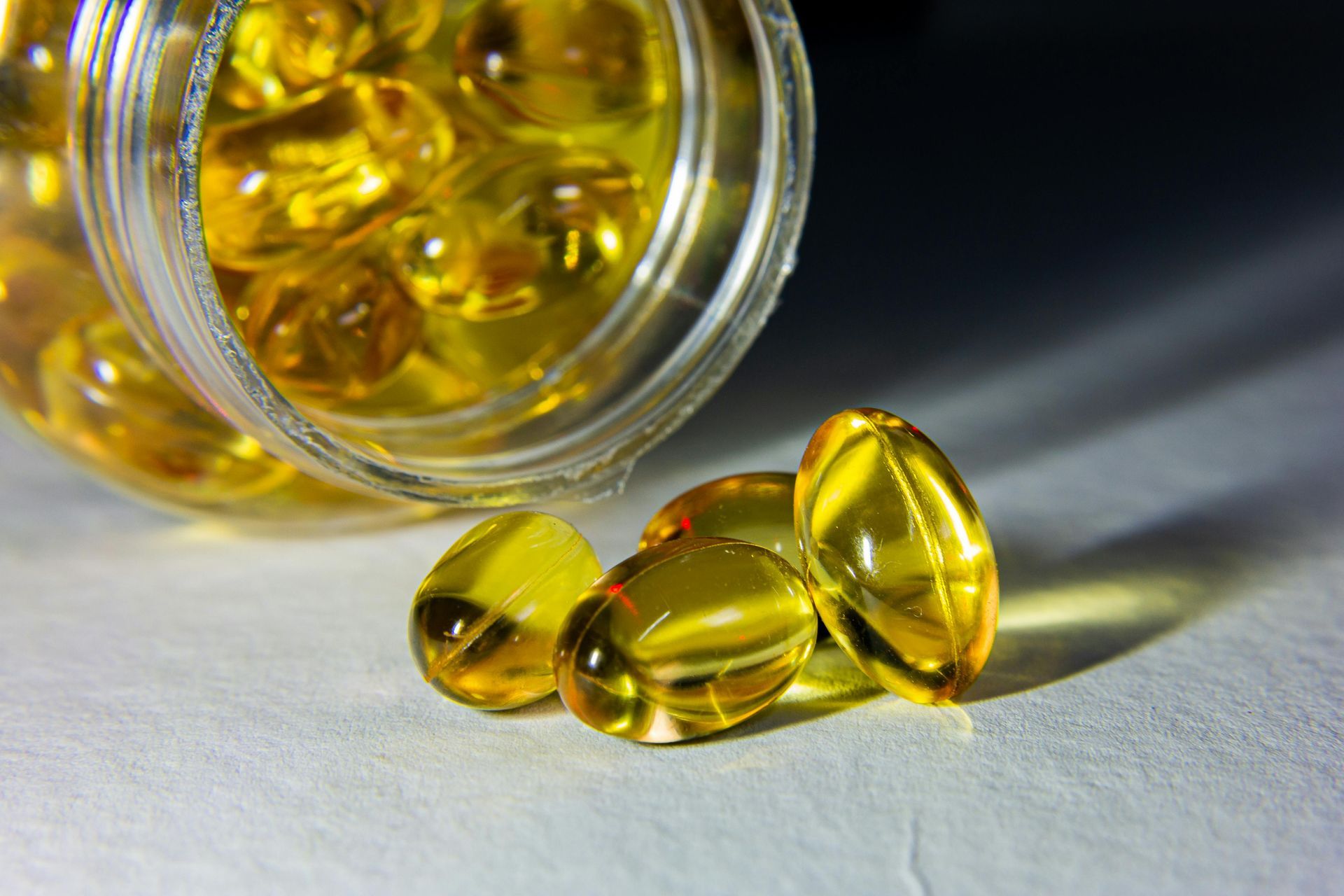 A glass bottle tipped over, spilling translucent golden gel capsules onto a white surface.