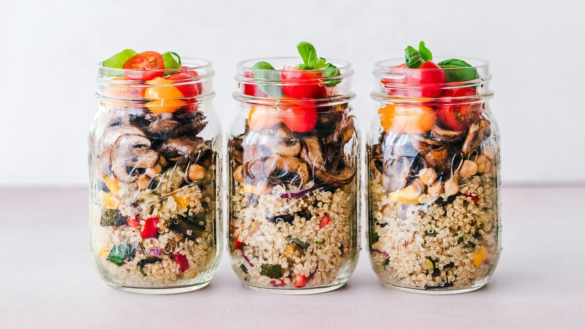 Three jars filled with rice and vegetables on a table.