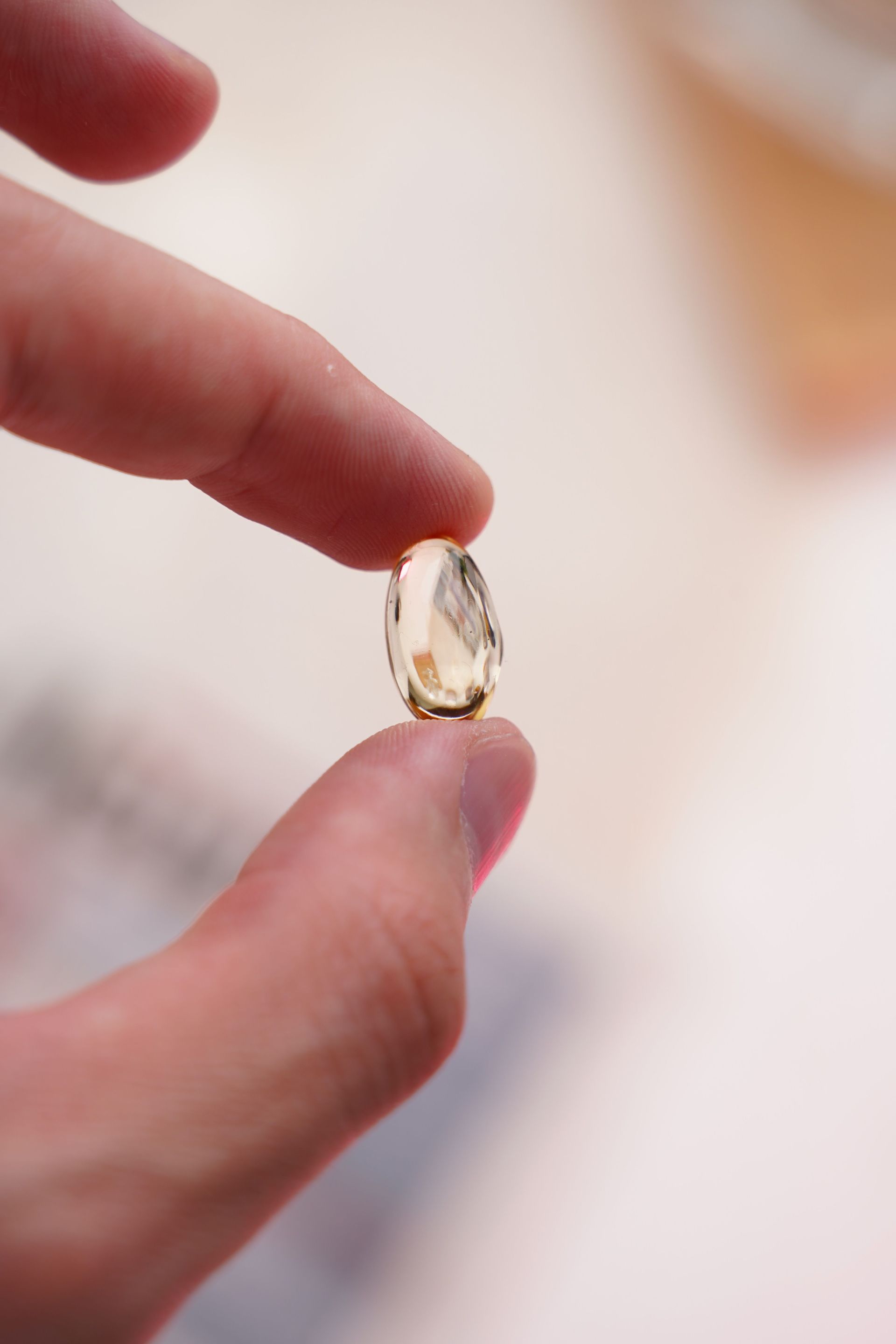 A hand holding a clear amber softgel capsule between two fingers.