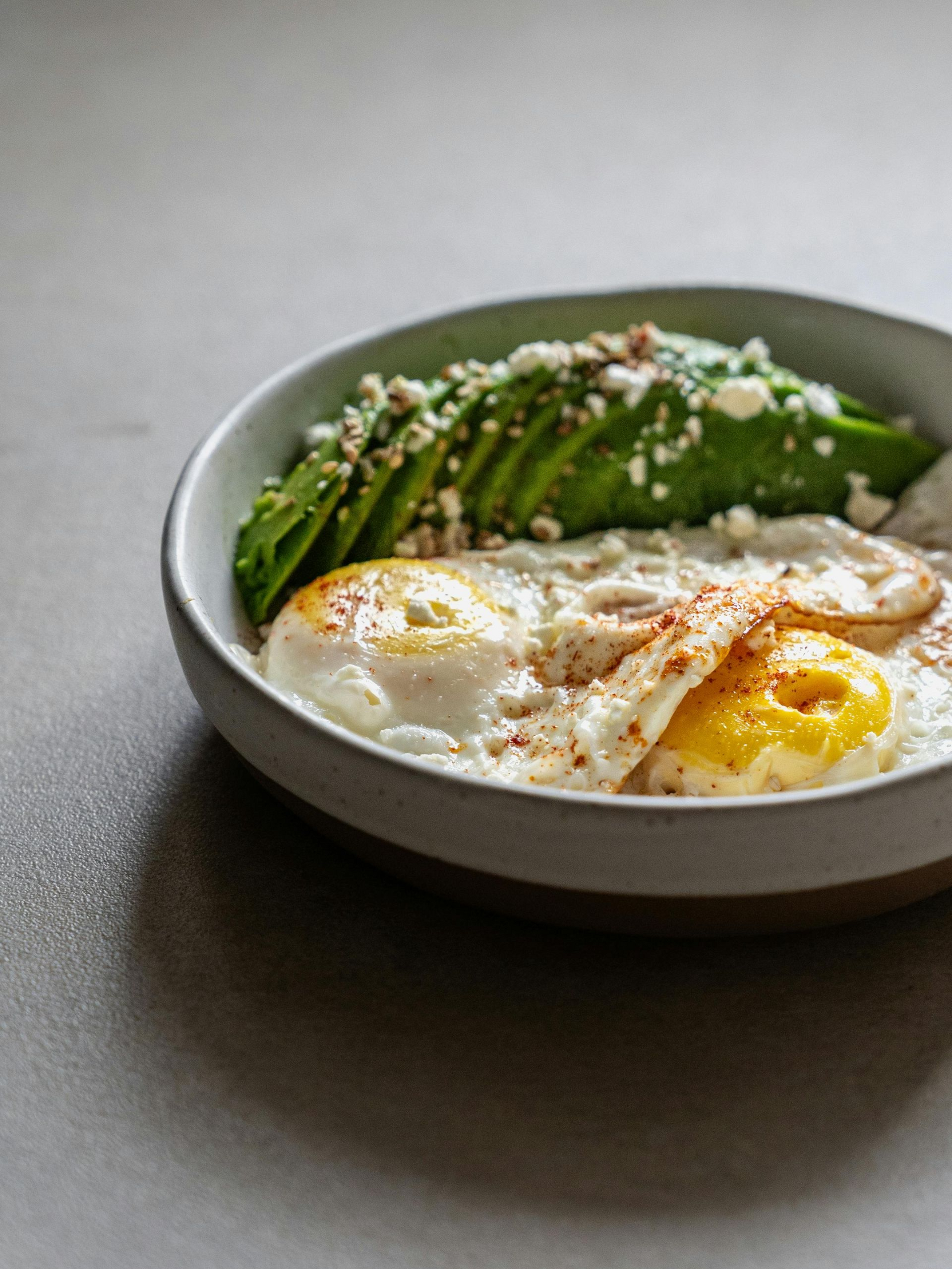 Bowl of sliced avocado with crumbled cheese, and two fried eggs sprinkled with paprika.