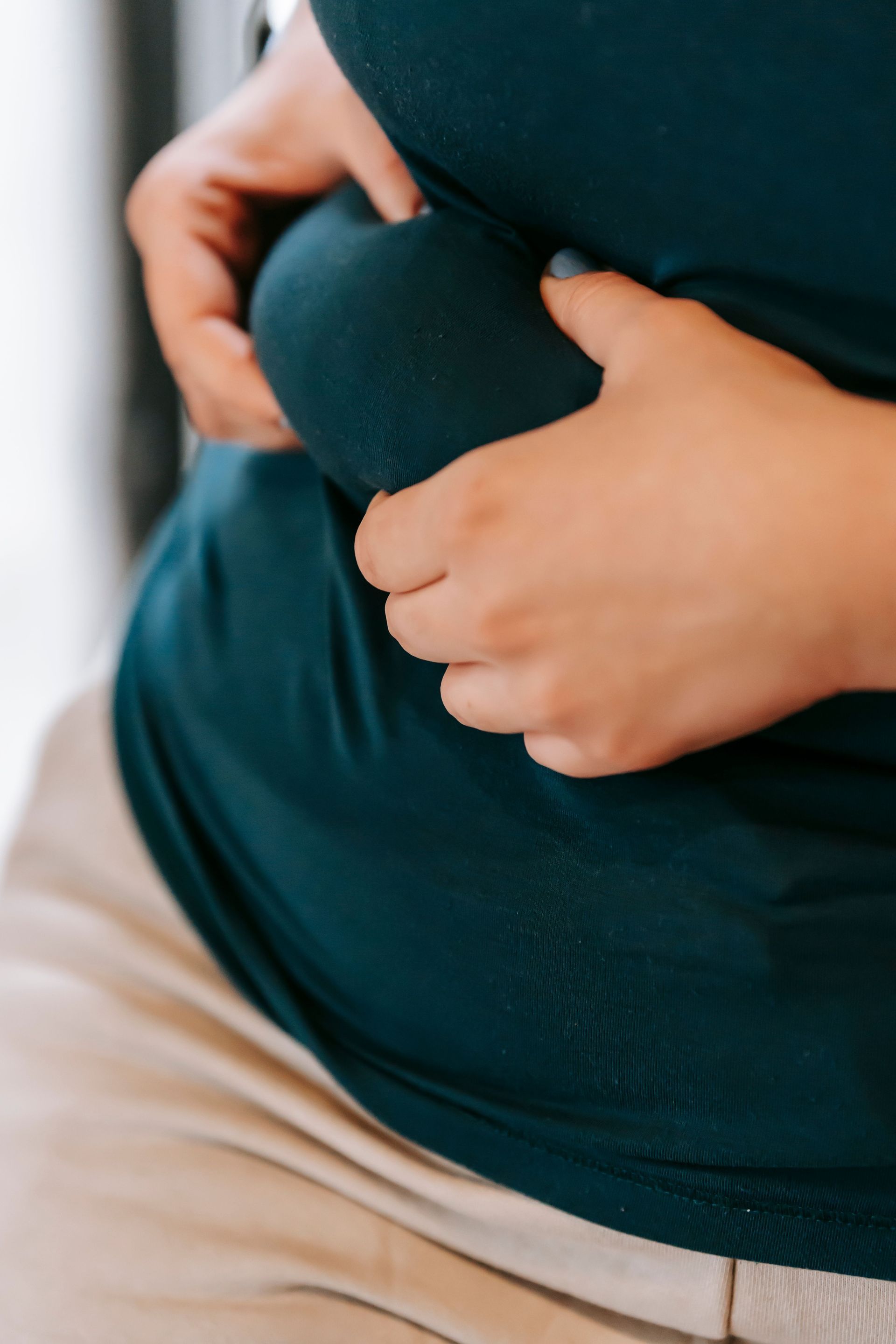 Hands holding a rounded belly over red shirt and plaid pants, suggesting pregnancy or stomach discomfort