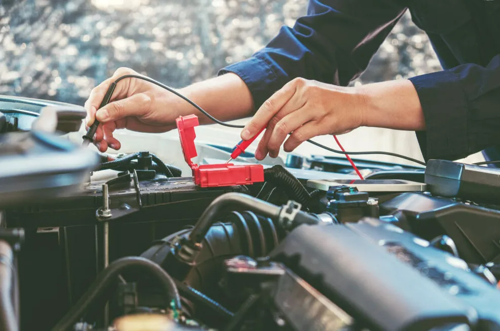 Hands Using a Red Battery Charger on a Car Engine in a Garage — Fischer Automotive in Svensson Heights, QLD