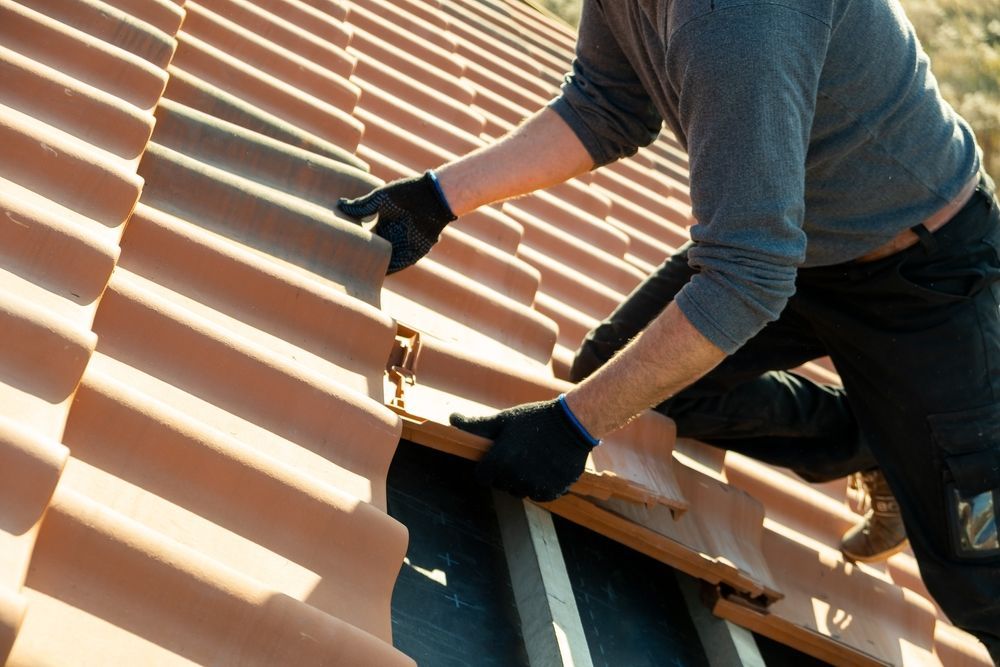 A Man is Installing Tiles on a Roof — RJT Roofing In Bonner, ACT