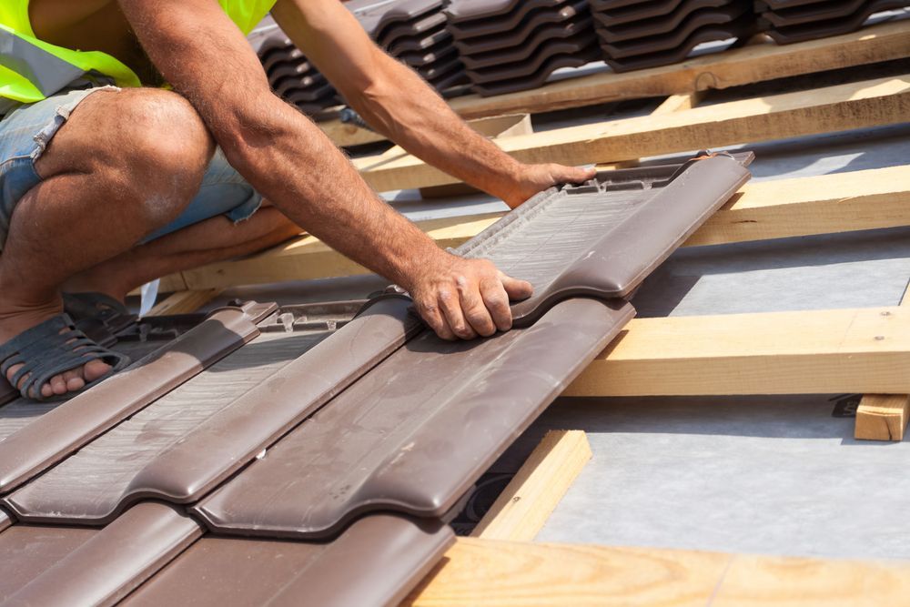 A Man is Laying Tiles on a Roof — RJT Roofing In Canberra, ACT