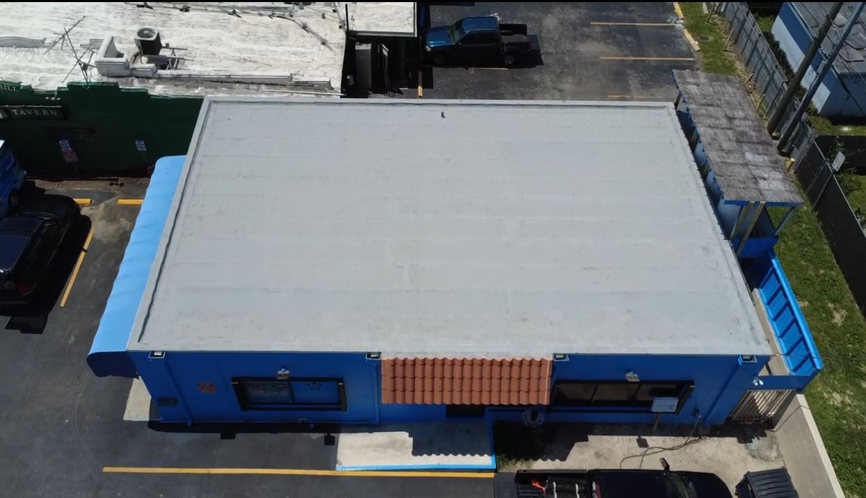 Overhead view of a blue building with a flat gray roof and a red tiled section.