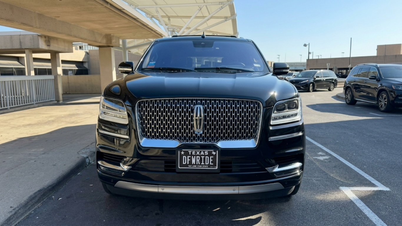 Man in suit carrying a brown briefcase steps from a black car outside a terminal entrance