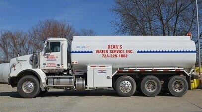 A large white water service truck parked outdoors with company branding and a phone number on it A large white water service truck parked outdoors with company branding and a phone number on it