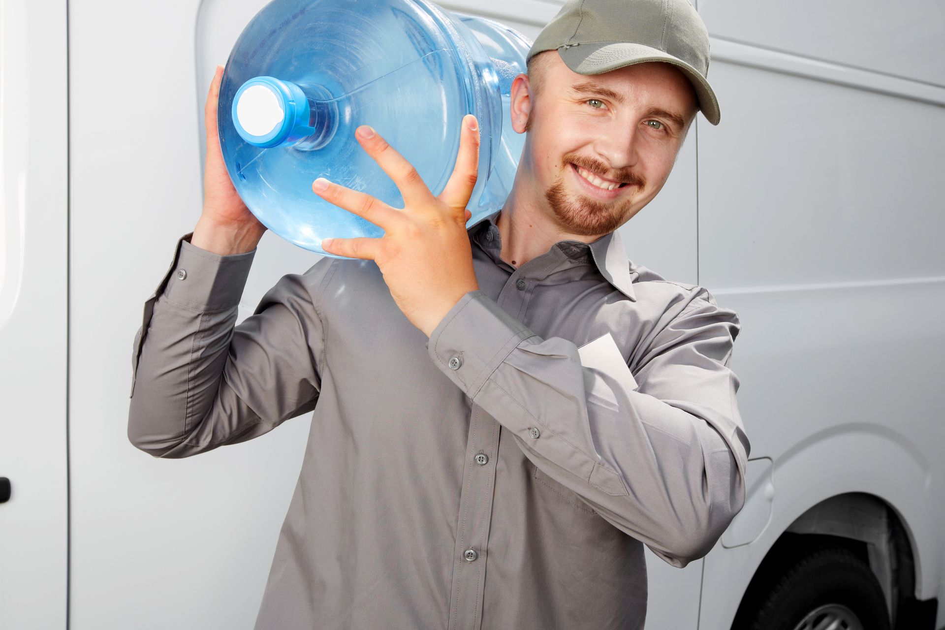 A male water delivery service worker smiles at the camera as he holds a bottle of drinking water. A male water delivery service worker smiles at the camera as he holds a bottle of drinking water.