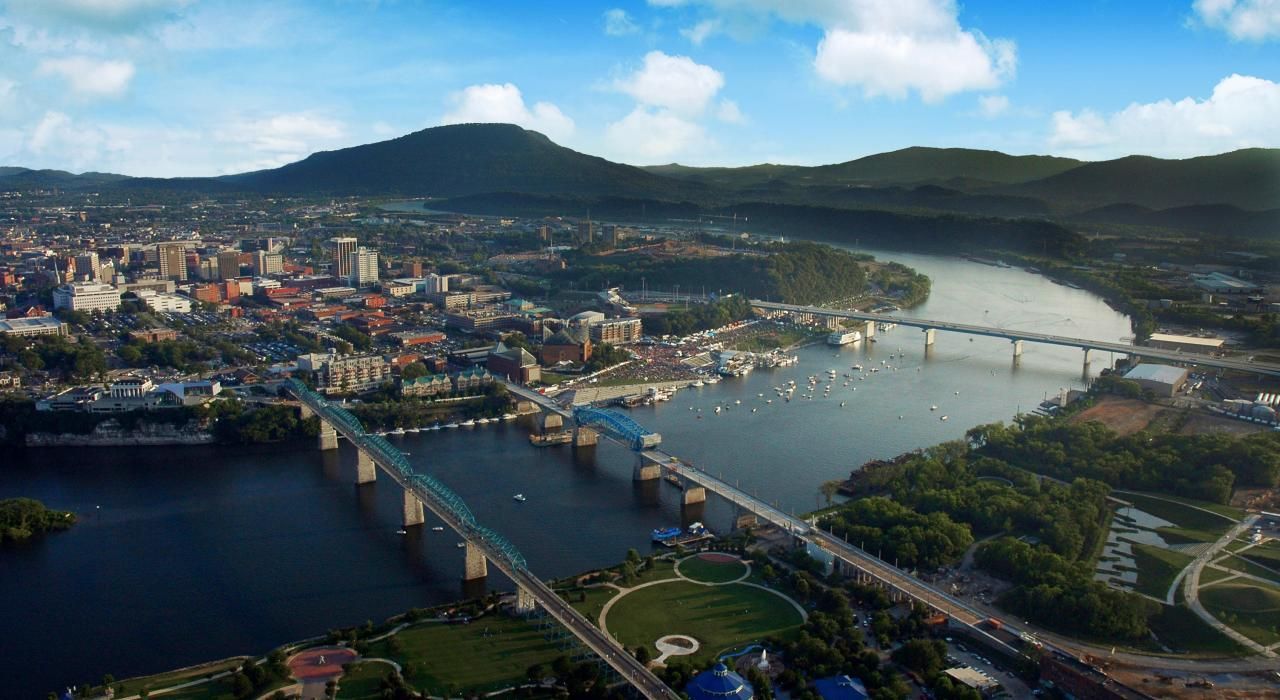 Aerial view of a city along a river with several bridges and hills in the background at sunset