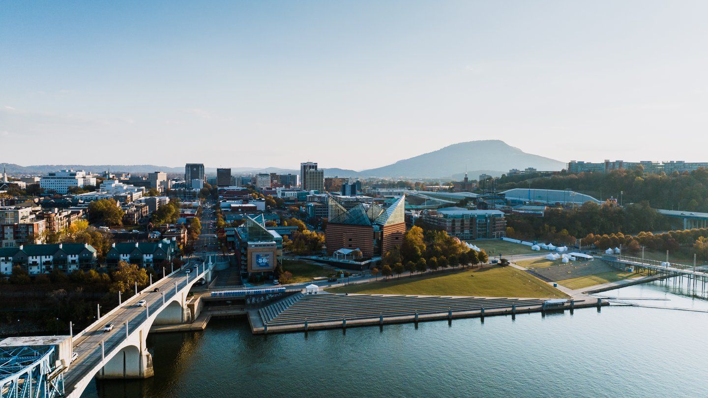 City skyline by a river at sunset, with a bridge in the foreground and a mountain in the distance