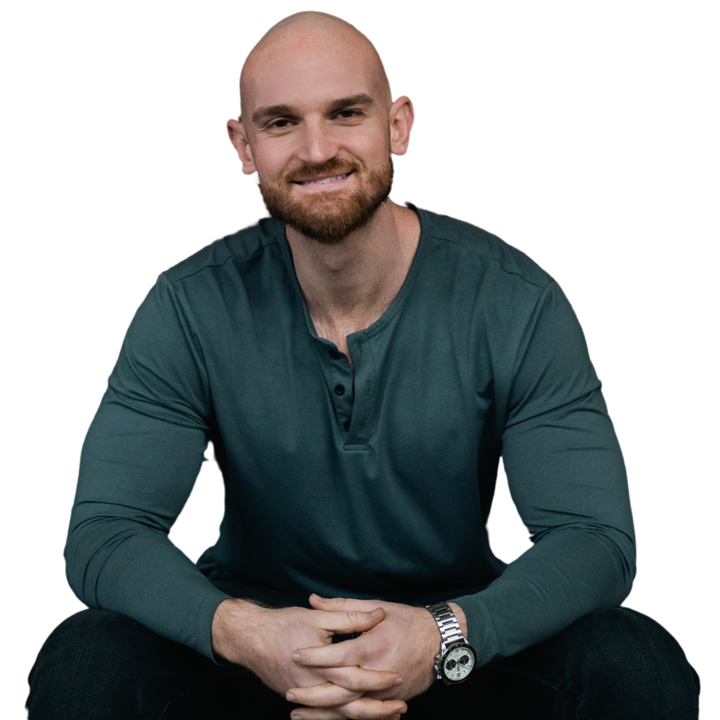 A bald man with a beard is sitting down with his hands folded
