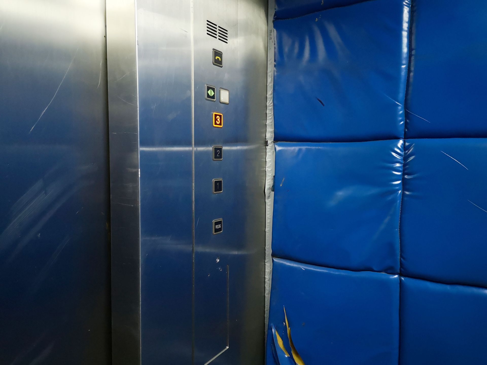 Stainless steel elevator panel next to blue padded wall panels