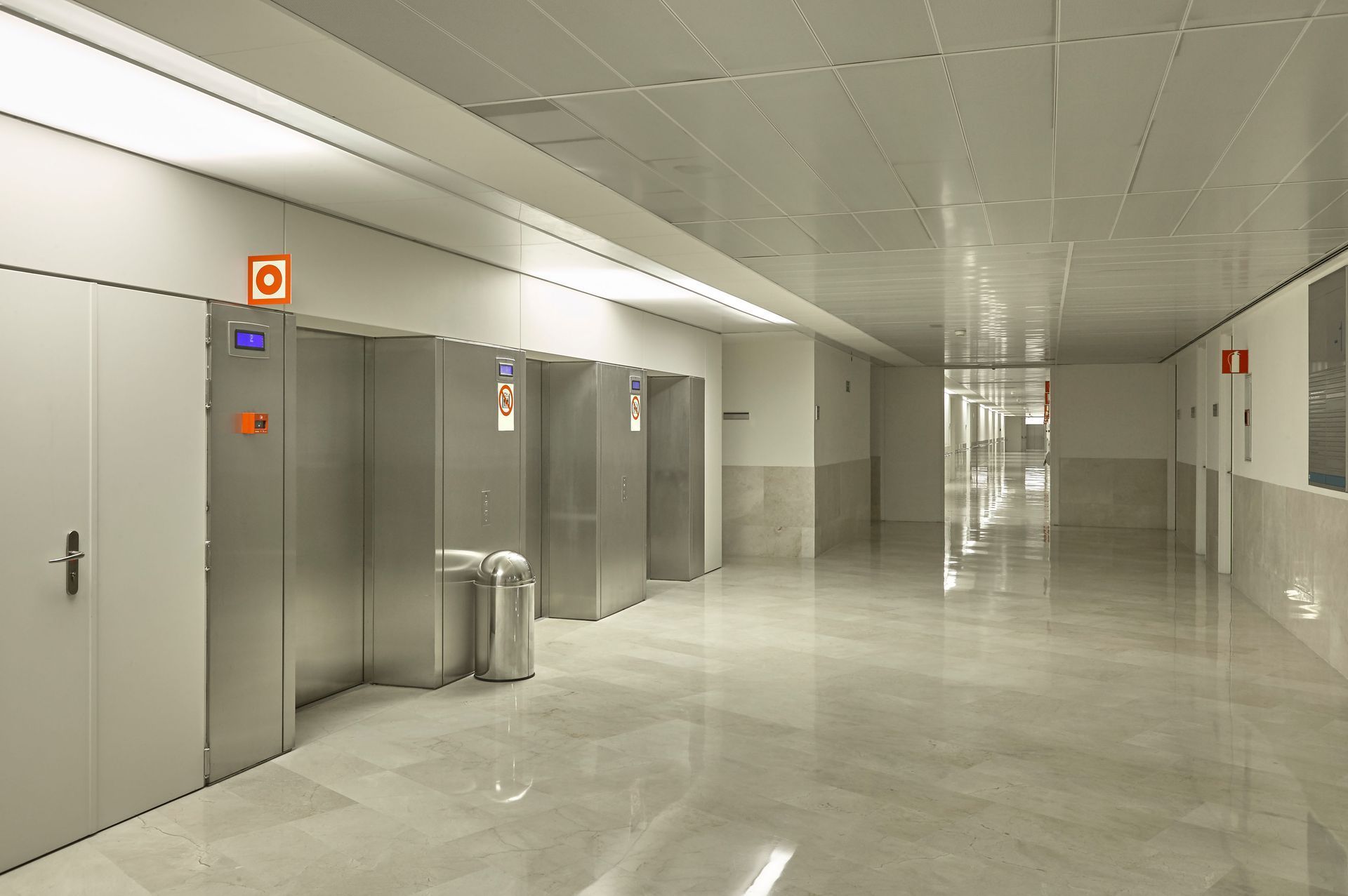 Empty modern hallway with elevators, gray doors, and polished floors