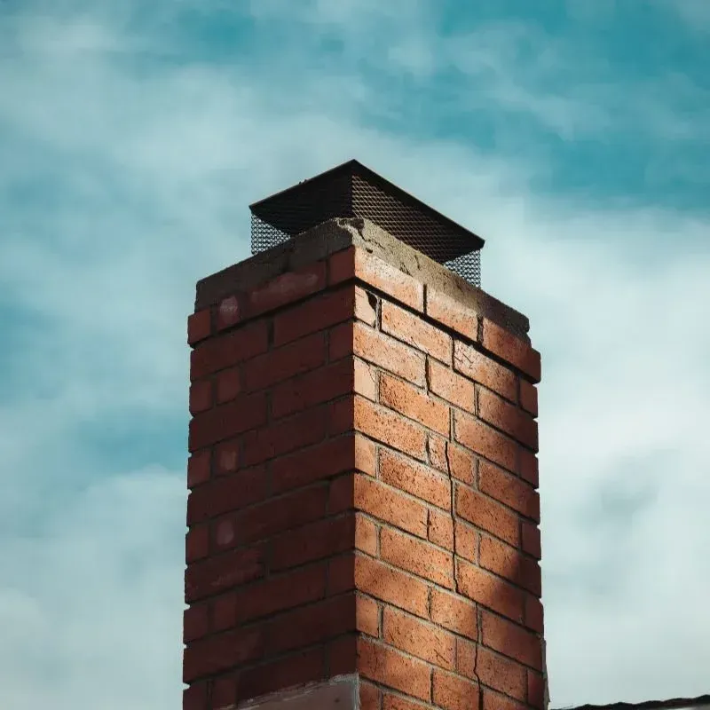 A brick chimney against a blue sky with clouds.