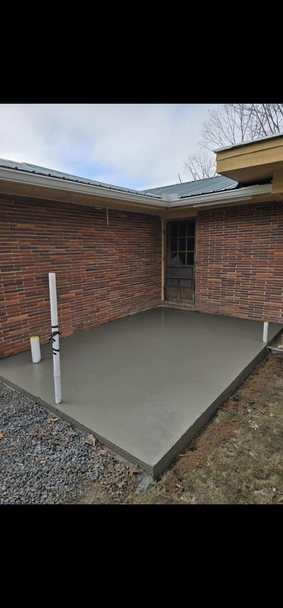 Concrete patio beside brick house with a white handrail and gravel yard