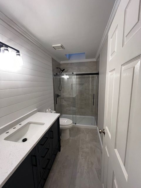 Narrow bathroom with white vanity, dark cabinets, toilet, and glass shower enclosure