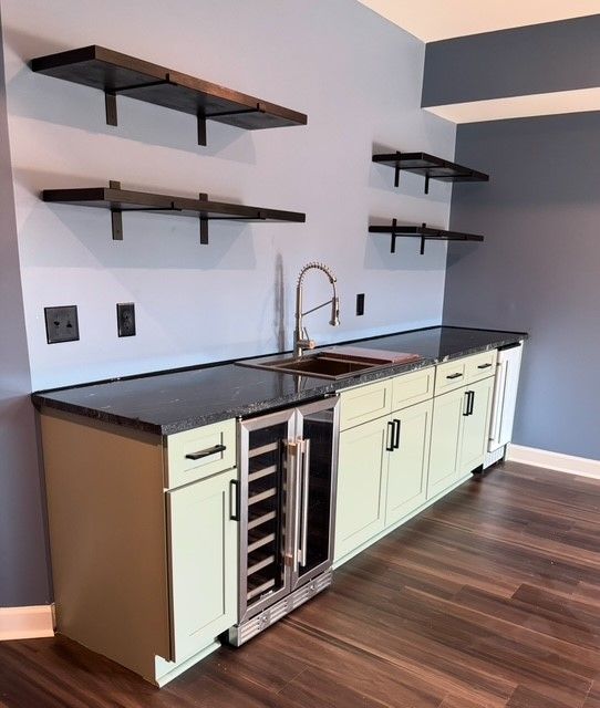 Modern kitchen with black countertops, pale cabinets, wall shelves, and a sink with a wine cooler.