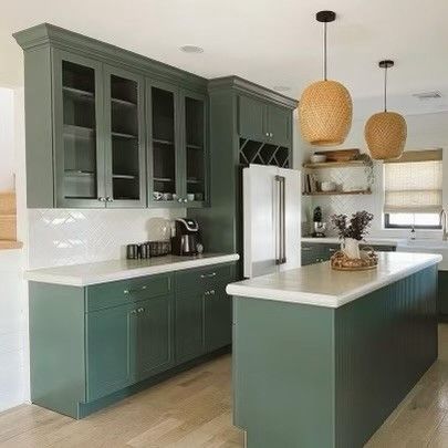 Modern kitchen with green cabinets, white countertops, island, pendant lights, and stainless steel fridge.
