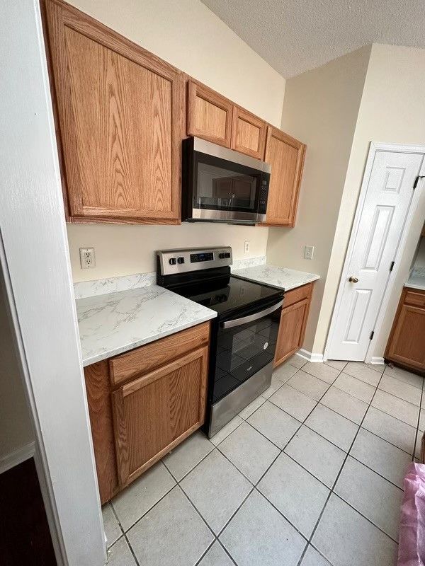 Small kitchen with wood cabinets, black stove, light countertops, and white tile floor.