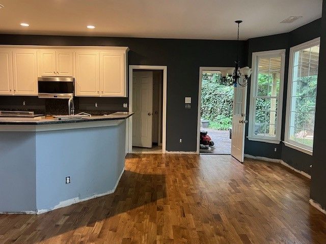 Open kitchen and living area with hardwood floors, blue accent wall, and large windows overlooking greenery